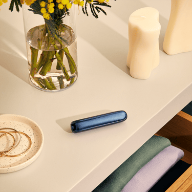 Ploom AURA device resting on a table with Navy Blue Augmented Pattern front panel attached, blending seamlessly into a clean, everyday setting.
