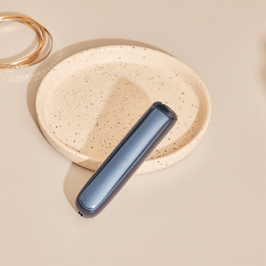 Ploom AURA device positioned on a table featuring a Navy Blue Augmented Pattern front panel, drawing attention to its balanced form and rich finish
