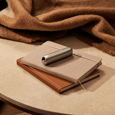 Ploom AURA front panels with Lunar Silver Augmented Pattern placed on stacked notebooks, creating a creative lifestyle scene with modern appeal.
