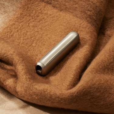 Ploom AURA device with Lunar Silver front panel placed on a maroon blanket, blending soft textures with a sleek, contemporary metallic finish.
