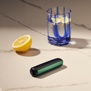 Ploom AURA front panel Amazon Green on a table, catching light across curves, emphasizing glossy finish, vibrant tone, and refined, playful design.
