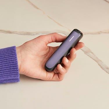 Tangan memegang Ploom AURA dengan panel Lavender, menekankan modulariti, warna ceria dan gaya peranti yang dipersonalisasi.