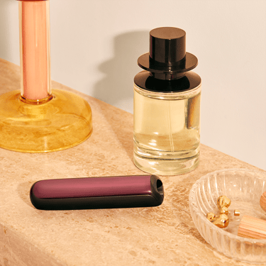 Peranti Ploom AURA dengan panel hadapan Dark Orchid di atas meja solek, menggambarkan gaya hidup moden yang bergaya.