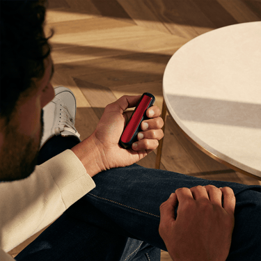 Seorang lelaki memegang peranti Ploom dengan panel Lava Red, menunjukkan aksesori menambah aksen berani sambil kekal elegan dan mudah digenggam.
