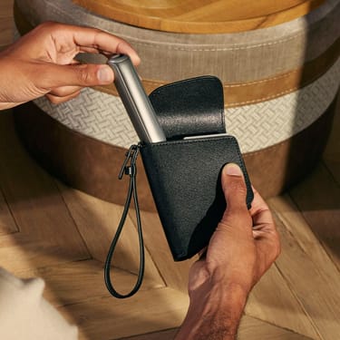 Tangan mengeluarkan peranti Ploom AURA daripada Jet Black Duo Carry Case, menunjukkan akses mudah dan rekaan storan praktikal.