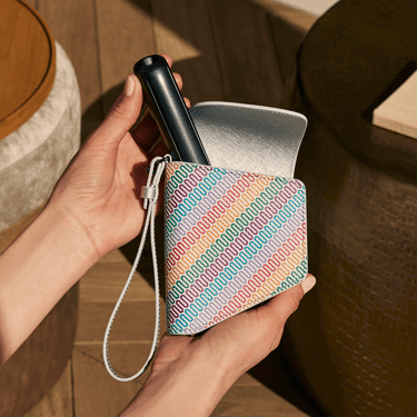 Tangan mengeluarkan Ploom AURA daripada Duo Carry Case Multicolored Patterned Canvas, menonjolkan akses pantas dan praktikal.