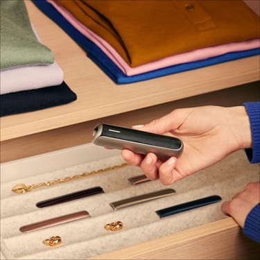 Hand holding Ploom AURA Jet Black Augmented Pattern panel, showing compact ergonomic design, smooth grip, and stylish presence in daily use.
