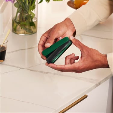 Tangan memasang Amazon Green Back Cover pada peranti Ploom AURA, merakam detik mudah personalisasi keperluan harian.
