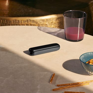 Ploom AURA Jet Black resting on a table, styled as a discreet companion with modern design and minimal visual presence.
