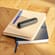 Ploom device with Jet Black Back Cover on top of a stack of notebooks, highlighting a clean, sophisticated look for everyday use