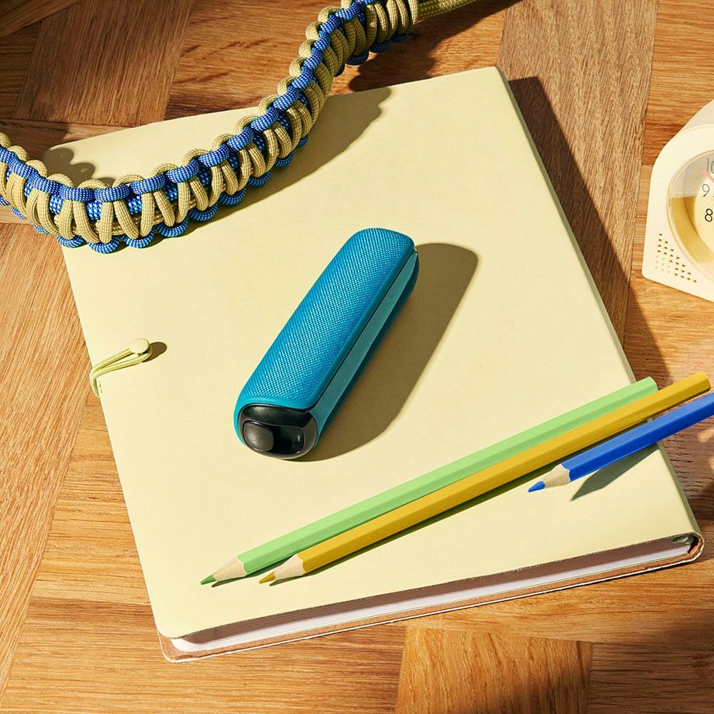 Ploom device with Ocean Blue Back Cover resting on a notebook, adding a calm accent to study, work, or creative moments.
