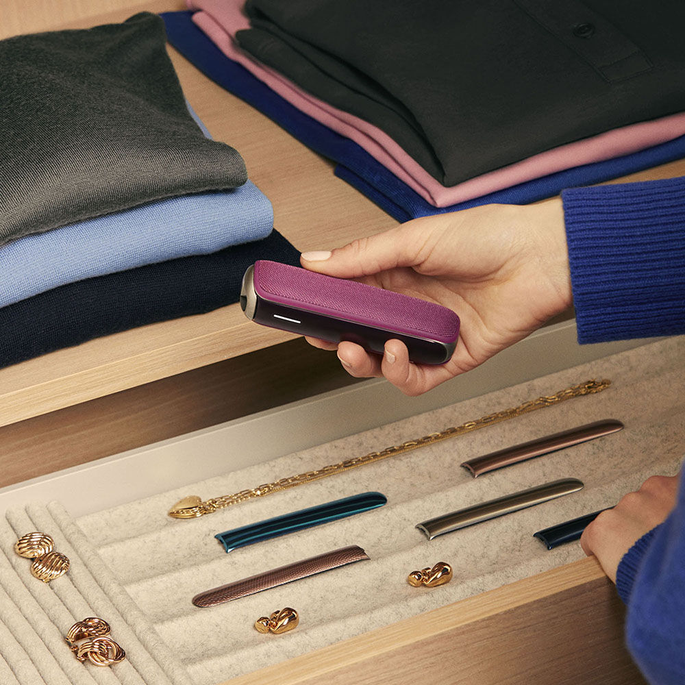 User pulling out a Dark Orchid Ploom AURA device from a drawer, capturing an intimate daily routine accented by a bold color choice.
