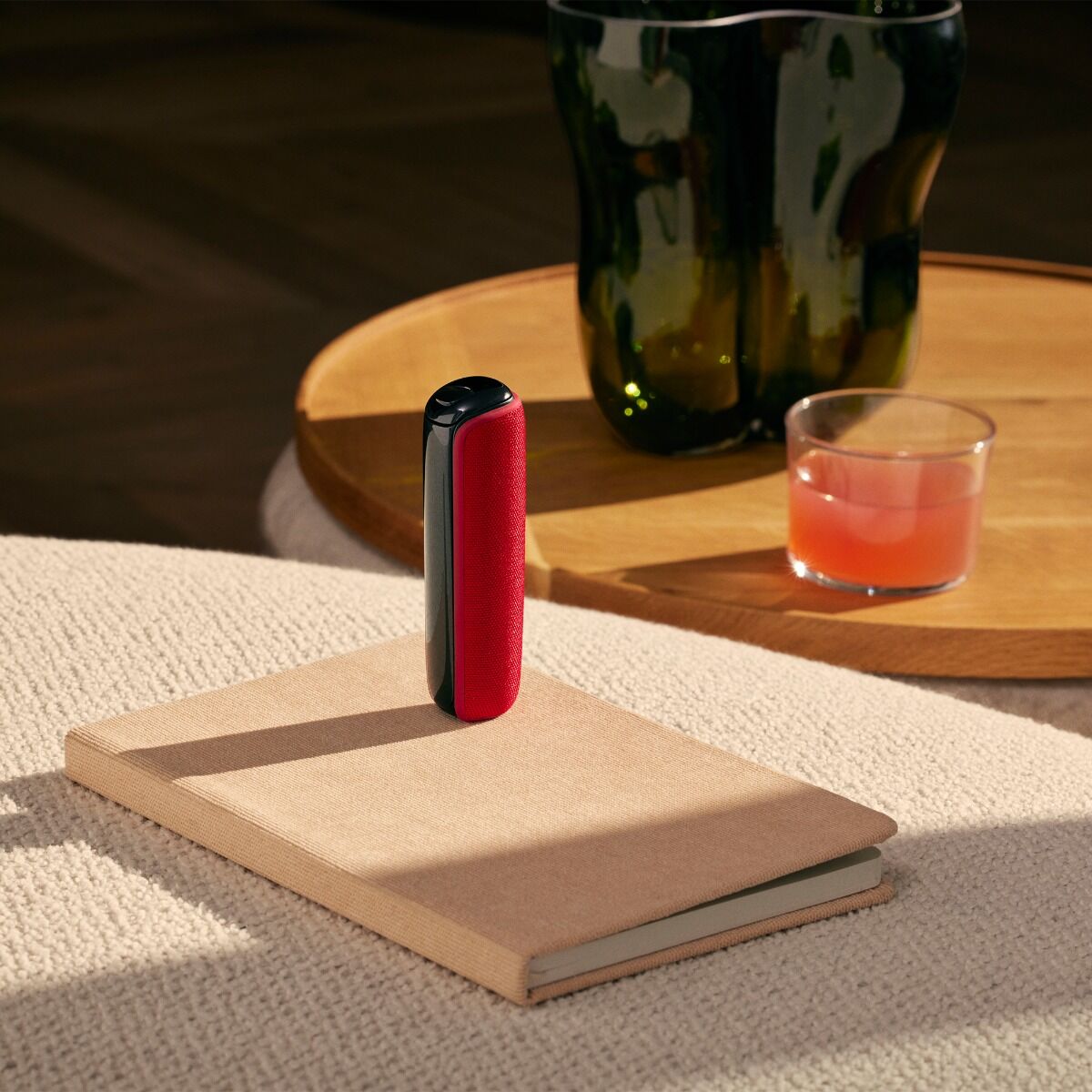 Ploom device with Lava Red Back Cover resting on a book on a table, blending bold color with warm tones and a calm lifestyle setting
