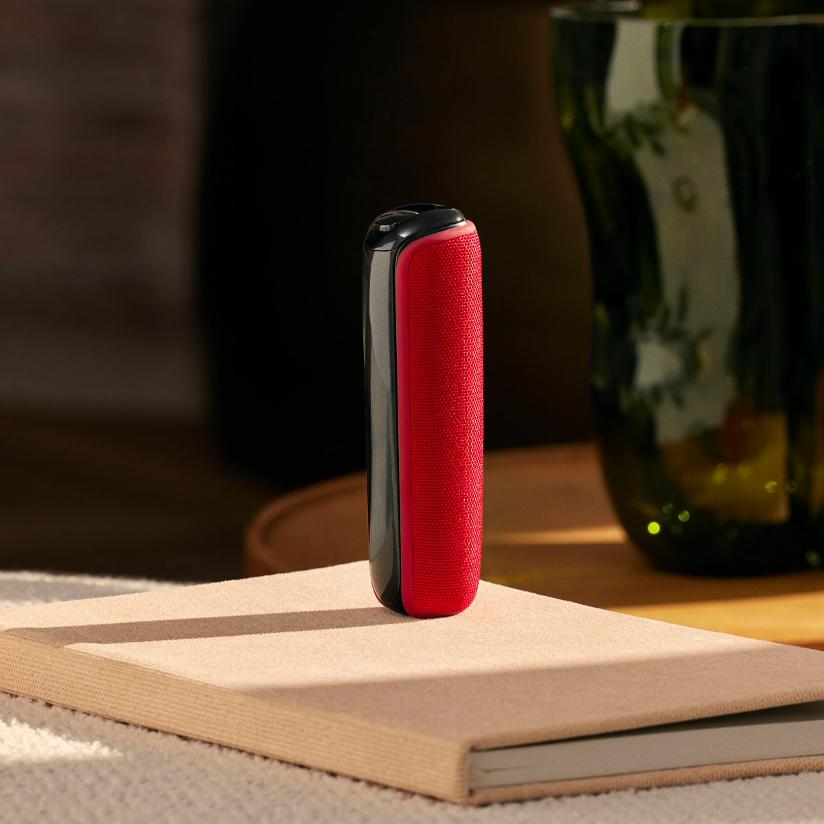 Ploom device with Lava Red Back Cover placed standing on top of a book, adding a bold accent to a relaxed moment at home or work
