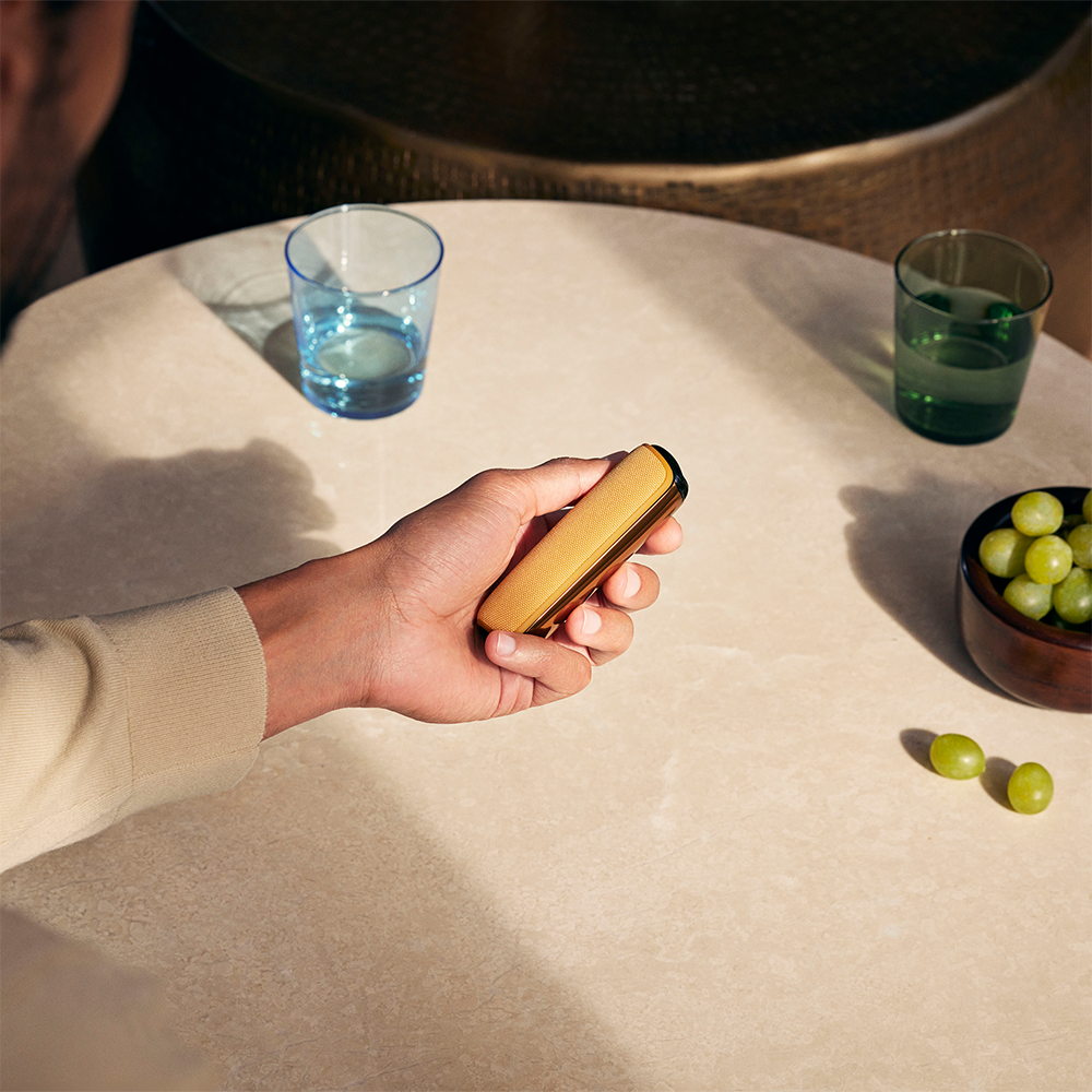 Tangan memegang peranti Ploom AURA dengan penutup Mango Sorbet terpasang, menunjukkan kesesuaian sempurna, warna ceria dan rekaan ergonomik.
